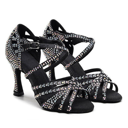 A pair of black strappy high-heeled dance shoes embellished with iridescent rhinestones, shown against a plain white background.